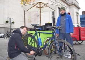 A mechanic and a member of the public work together to repair a bike outside the town hall